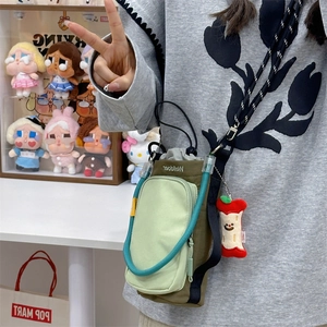 Detail of green bicolor crossbody bag with blue rope handle and red apple plush charm