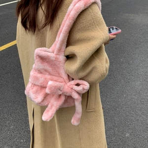 Detail of pink plush shoulder bag with a large bow shown on a model in street style