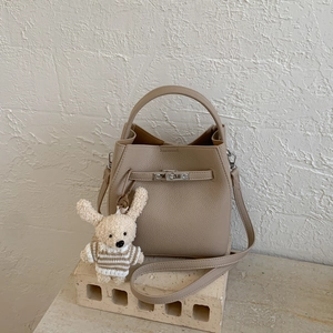 Close-up of beige lychee grain bucket bag with silver twist lock and plush bear charm