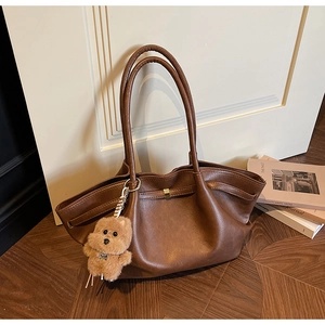 Close-up of brown leather tote bag with gold metal buckle and cute bear pendant