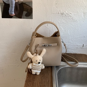 Detail of beige bucket bag featuring lychee texture and cute plush rabbit charm