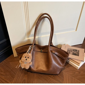 Detail of dark brown faux leather tote bag with plush bear charm on wooden floor