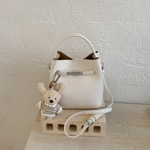 Close-up of white lychee leather bucket bag with silver turn-lock and plush doll charm
