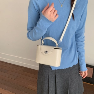 Detail of cream box bag with silver twist lock on blue sweater and grey pleated skirt