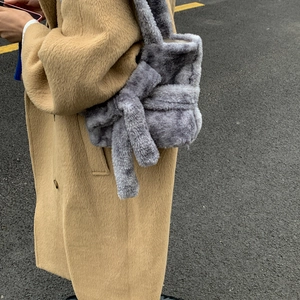 Detail view of a large grey faux fur tote bag with oversized knot accent on camel coat