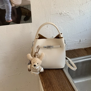 Detail of off-white bucket bag with pebble leather texture and cute bear charm