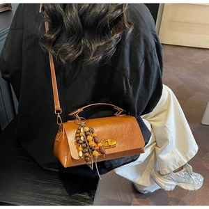 Detail view of brown faux leather crossbody bag with lychee texture and wooden bead charm
