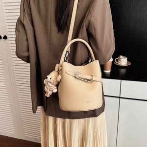 Detail der beigen Bucket Bag aus Leder mit Metallschnalle und süßem Bärenanhänger