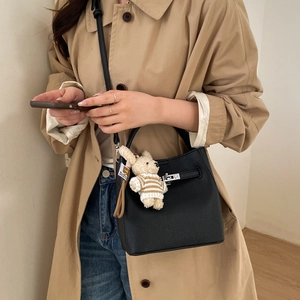 Detail of black pebbled leather bucket bag with silver buckle and bear charm on model