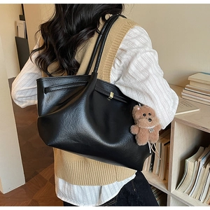 Macro view of black leather tote bag with soft lychee texture and plush bear pendant