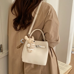 Detail of a beige pebbled leather bucket bag with a plush bear charm on a trench coat model