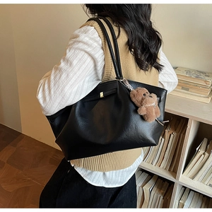 Detail of a black leather tote bag with a cute brown bear charm in a cozy library setting