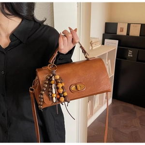 Close-up of brown retro leather handbag featuring colorful wooden bead charm decoration