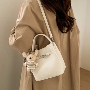 Detail of cream lychee texture leather bucket bag with silver turn-lock and bear charm