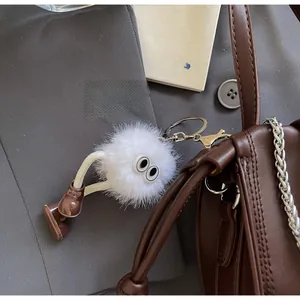 Detail of a fluffy white faux fur pompom keychain with cute eyes on a brown leather bag