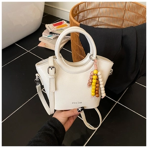 Detail of white bucket bag featuring beaded charm and textured faux leather surface