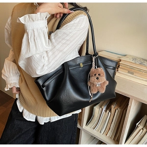 Close-up of black tote bag with pleat details and brown teddy bear charm on shoulder strap