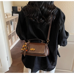 Detail of dark brown leather crossbody bag featuring a gold oval twist lock and wooden beads