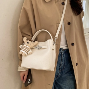 Detail of off-white bucket bag with pebble texture and silver lock featuring a bear charm