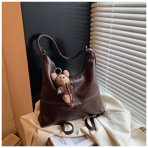 Detail of dark brown leather tote bag with white contrast stitching and a plush bear charm