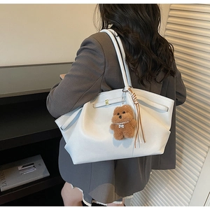 Detail of white leather tote bag with brown plush bear charm and leather tassel