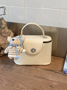 Off-white mini box handbag with silver twist lock and cute teddy bear charm on wood surface