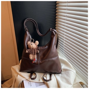 Detail of dark brown leather tote bag with white contrast stitching and plush bear charm