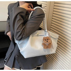 Detail view of large faux leather tote bag with golden lock and teddy bear charm