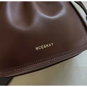 Detail of dark brown leather cloud bag with gold MCE&KAY branding and fine stitching