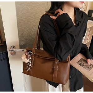 Detail of dark brown pebble leather shoulder bag with plush bear charm on model's shoulder