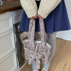 Detail of soft plush brown handbag with a large faux fur bow in a cozy home setting