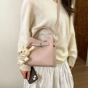 Close-up of pink lychee leather bucket bag with silver lock and plush bunny charm