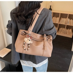 Detail of caramel leather tote bag with side buckles and cute plush bear charm