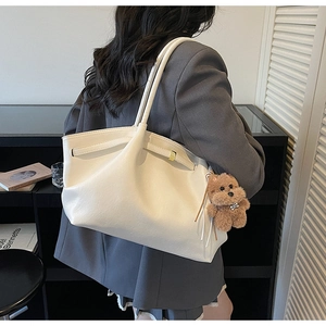 Detail of off-white leather tote bag with brown plush bear charm and long shoulder straps