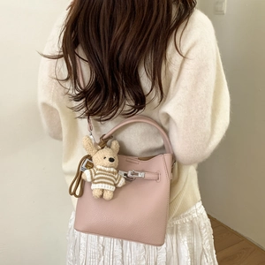 Detail of light pink pebble leather bucket bag with metal clasp and plush bear charm