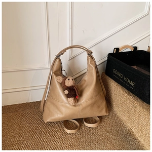 Detail of khaki leather hobo bag with teddy bear charm on woven carpet texture