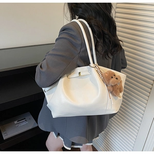 Detail of minimalist cream white tote bag with gold buckle and brown teddy bear charm