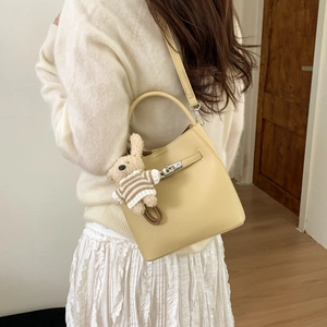 Detail of light yellow leather bucket bag with metal buckle and plush rabbit charm