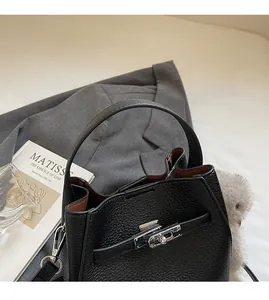 Detail of black pebbled leather bucket bag with silver metal turn-lock and wide top handle