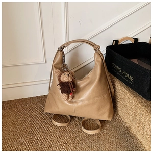 Detail of light brown faux leather tote with adjustable straps and a cute teddy bear charm
