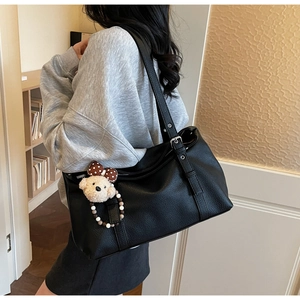 Close-up of black leather tote with adjustable strap and cute bear charm pendant