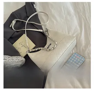 Sac demi-lune beige matelassé avec chaîne argentée posé sur une veste grise