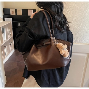 Detail view of a large brown faux leather tote bag with a plush bear charm accessory
