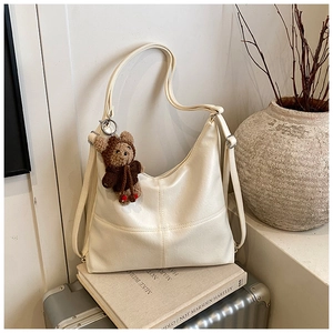 Detail of off-white PU tote bag with bear charm on travel suitcase and books