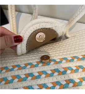 Detail of woven straw tote bag featuring golden magnetic clasp and striped fabric accent