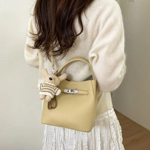 Detail of beige bucket bag with silver clasp and cute bear charm on model
