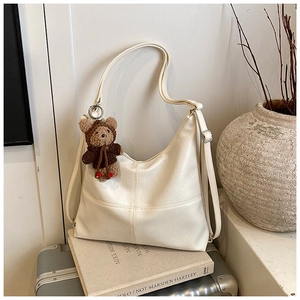 Detail of cream white tote bag with cross-stitch quilting and a cute teddy bear charm