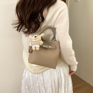 Detailed close-up of beige lychee grain leather bucket bag with metallic lock and puppy charm