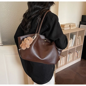 Detail view of large brown faux leather tote bag with cute plush bear charm accessory