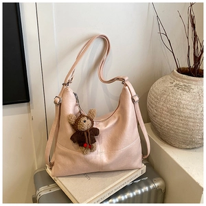Detail of pink faux leather half-moon shoulder bag with plush bear charm on suitcase